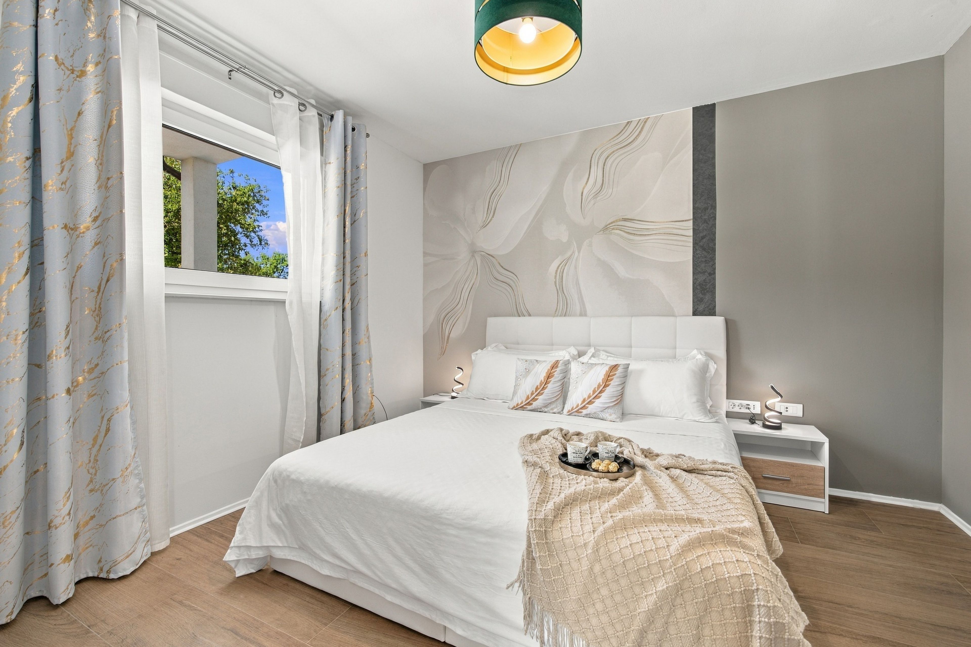 A modern bedroom with a large bed, a bedside table, a nightstand, and a window with curtains.