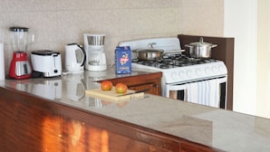 Una cocina equipada con estufa, tostadora, licuadora, cafetera y tabla de cortar con manzanas.
