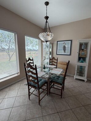 A dining area with a glass-top table, wooden chairs, and a chandelier.
