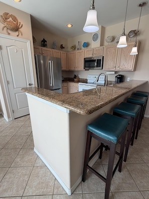 A kitchen with a central island, stainless steel appliances, wooden cabinets, and bar stools.