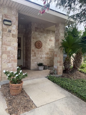 A stone house entrance with a number '31' on the wall, a potted plant, and a small statue.