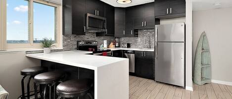 A modern kitchen with dark cabinets, a stainless steel refrigerator, a microwave, and a large window.