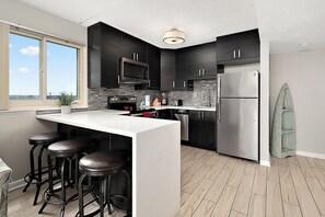 A modern kitchen with dark cabinets, a stainless steel refrigerator, a microwave, and a large window. - 2BR Atlantis Oceanfront Condo, Outdoor Pool (Ocean City)