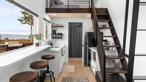 Een moderne keuken met een centraal eiland, een eethoek met barkrukken, een trap en uitzicht door grote ramen.