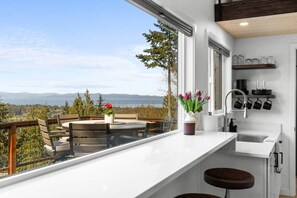 Une cuisine moderne dotée d’une grande fenêtre, un coin repas avec une table et des chaises, et une vue sur les montagnes.