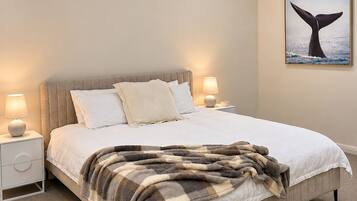 A bedroom with a bed, a ceiling fan, bedside lamps, a nightstand, and a wall-mounted picture of a whale tail.