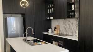 A modern kitchen with a central island, dark cabinetry, a stainless steel refrigerator, and a marble backsplash. - SAND -  Walk to Marina I Bay Views I 2 Master Suites (Nelson Bay)