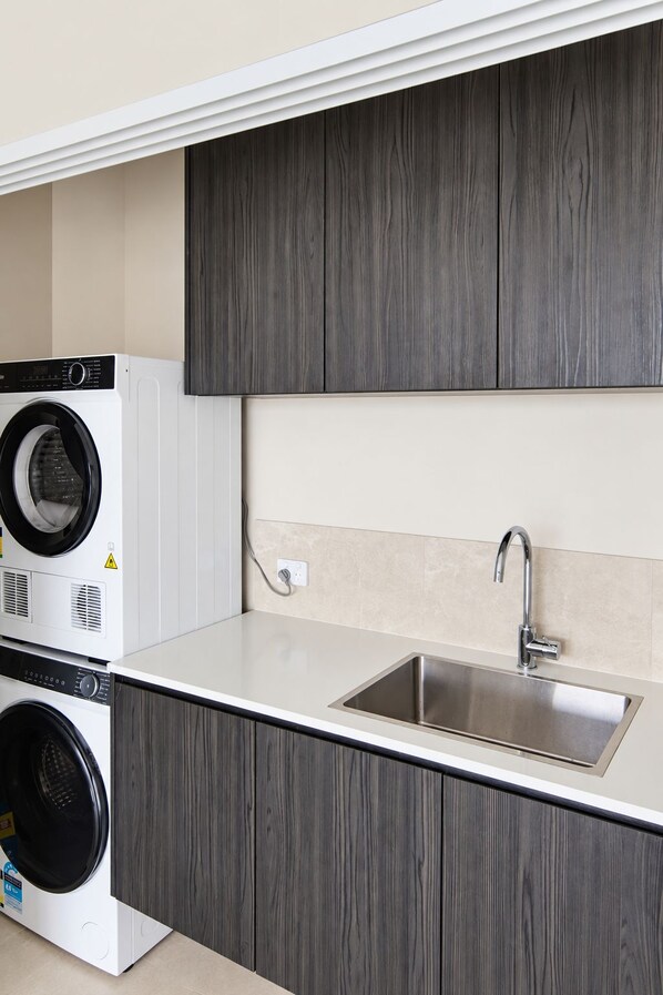 Una cocina compacta con lavadora y secadora integradas, un lavamanos de acero inoxidable y armarios de madera oscura.