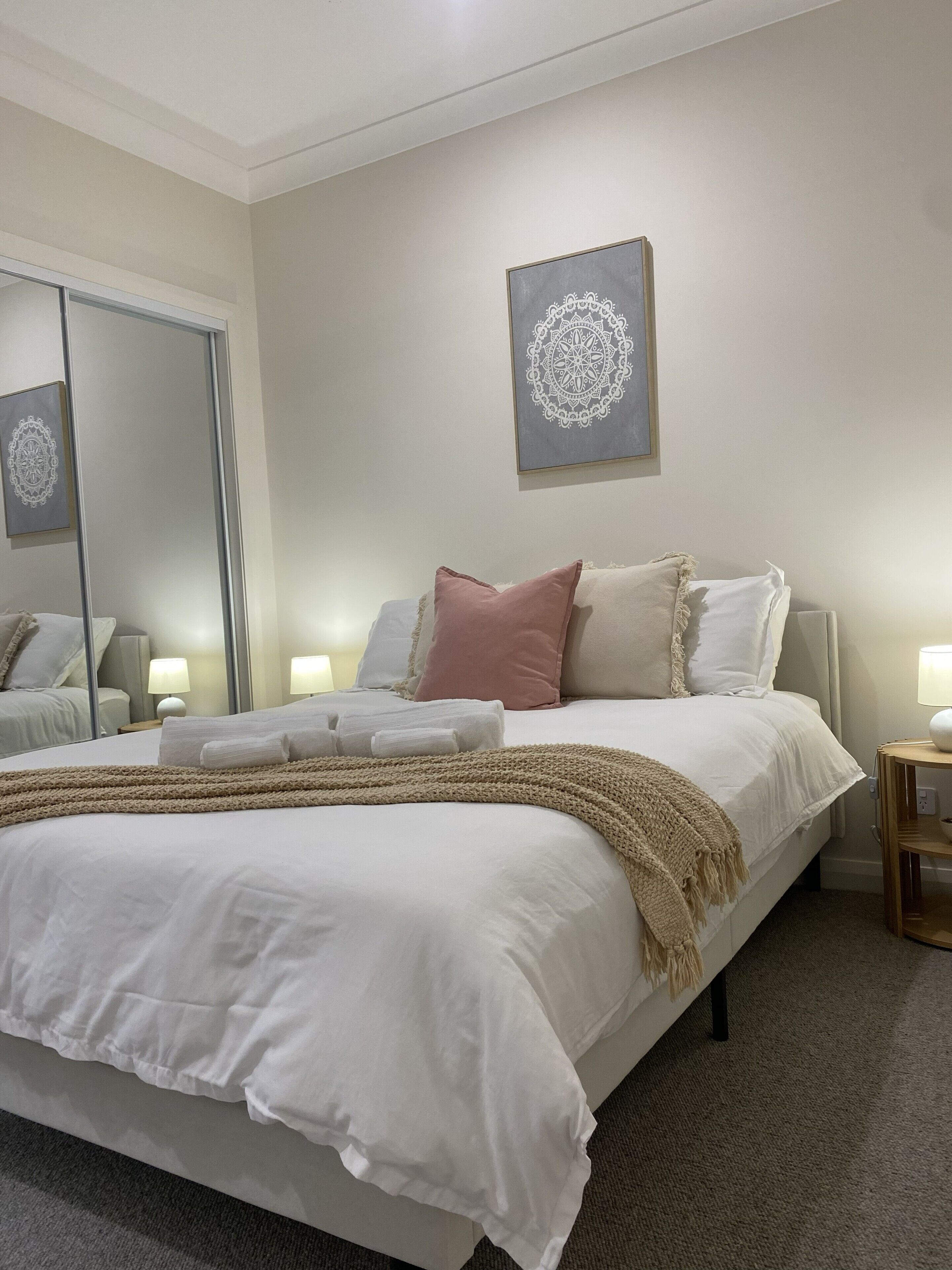 Een slaapkamer met een groot bed, bedlampen, een spiegel en een kunstwerk aan de muur.