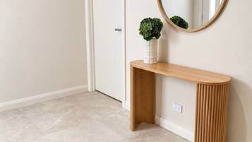 Un couloir avec une console en bois, un miroir rond et un tapis tissé.