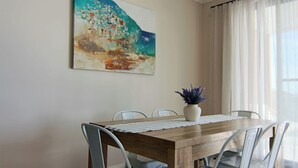 A dining area with a wooden table, white chairs, a potted plant, and a painting on the wall. - SAND -  Walk to Marina I Bay Views I 2 Master Suites (Nelson Bay)