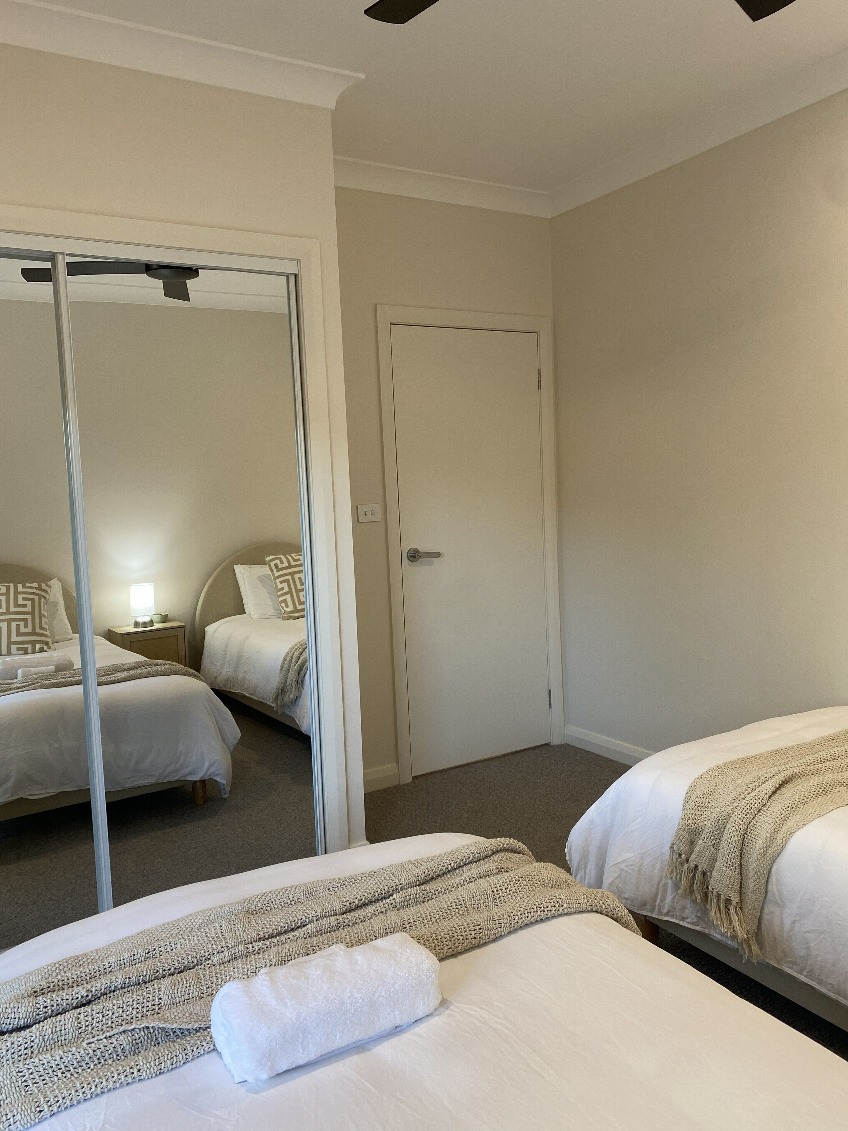 Habitación de hotel con dos camas, un espejo grande, una puerta y una mesita de noche con lámpara.