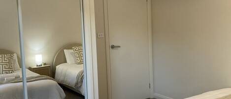 Habitación de hotel con dos camas, un espejo grande, una puerta y una mesita de noche con lámpara.
