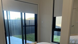 A bedroom with a large bed, a window, and a sliding glass door leading to a backyard. - SAND -  Walk to Marina I Bay Views I 2 Master Suites (Nelson Bay)