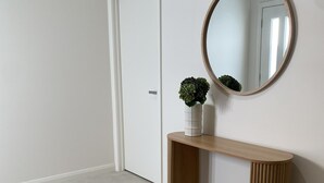A hallway with a wooden console table, a round mirror, a potted plant, and a woven rug. - SAND -  Walk to Marina I Bay Views I 2 Master Suites (Nelson Bay)