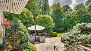 Eine Terrasse mit Steinboden, Gartenmöbeln und einem Grill.