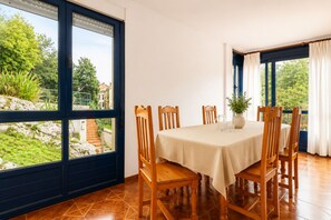 Uma área de refeições com uma mesa posta para quatro pessoas, janelas amplas com cortinas e vista para o verde lá fora.