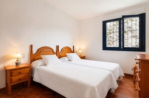 A double bed with a wooden headboard, two bedside tables with lamps, a dresser, and a window with a view of rocks. - House near Barro Beach Llanes | El Sumidoriu (Barro (Llanes))