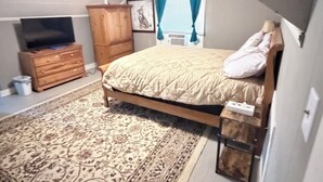 Une chambre à coucher comprenant un lit, une commode en bois, un téléviseur, un ventilateur de plafond et un tapis à motifs.