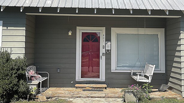 Une maison avec une porte rouge, une porte de garage et un porche avec deux chaises.