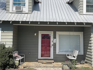 A house with a red door, a garage door, and a porch with two chairs.