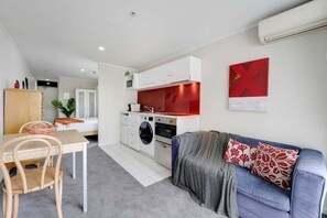 Un espace de vie compact comprenant un coin cuisine, un coin repas et un espace détente avec un canapé et des coussins.