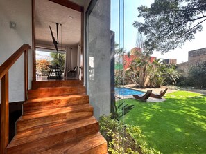A modern staircase leading to a room with a large window overlooking a swimming pool and garden. - Family Home with Pool and Palapa - Central and Quiet Location. (Cuernavaca)