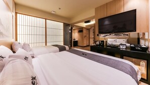 Habitación de hotel con dos camas, televisión, escritorio con teléfono y puerta corredera que da a un baño.