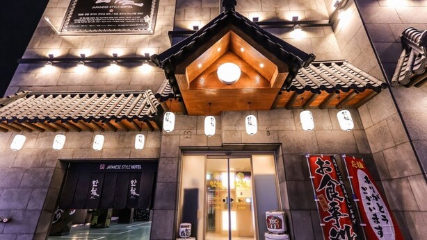 Entrada de un hotel de estilo japonés con arquitectura tradicional, que incluye un tejado de tejas y detalles de madera.
