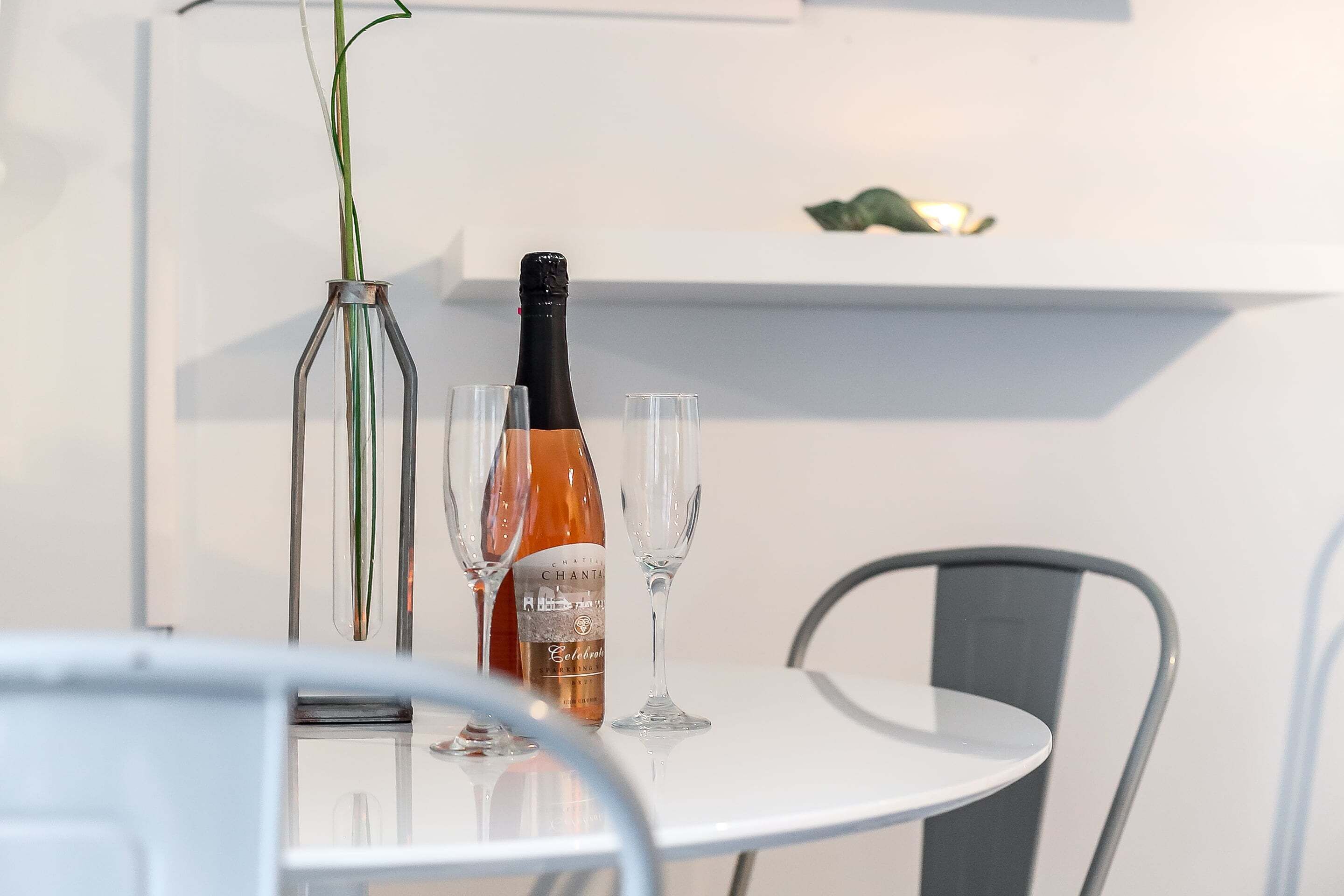 A table with a bottle of wine, two glasses, and a vase with a plant.