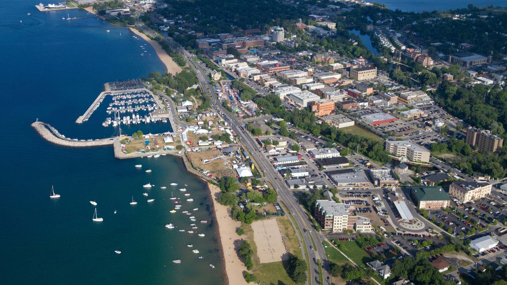 An aerial view of a coastal town with a marina, buildings, and roads.