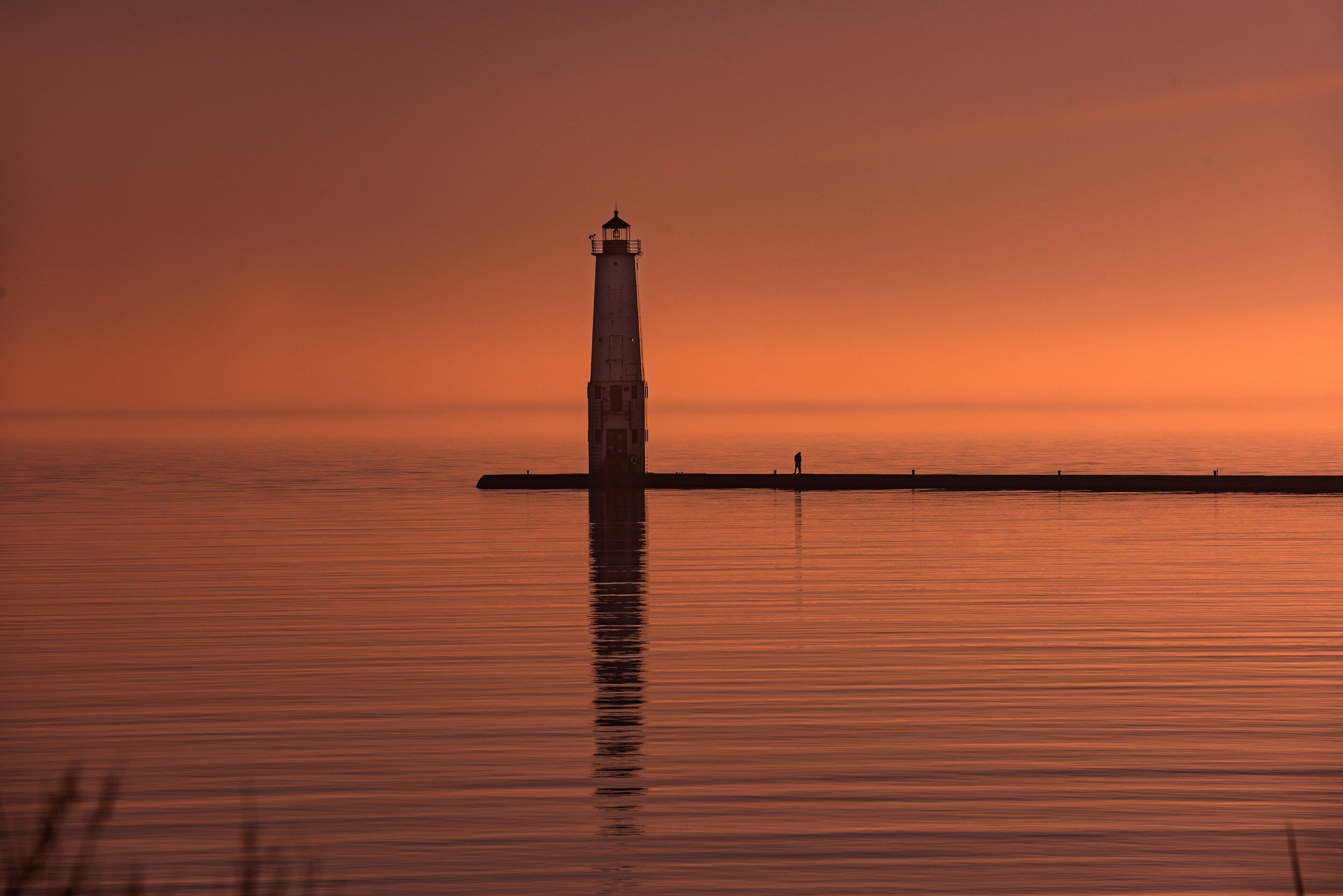 A lighthouse at sunset with calm water reflecting its image.
