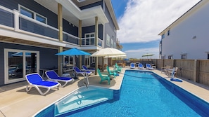 Piscina con sillas de descanso y sombrillas, rodeada por una terraza de madera y un edificio con ventanas grandes.