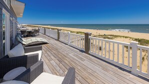 Een houten terras met rieten meubels, een witte balustrade en uitzicht op het strand.