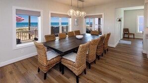 Een eetgedeelte met een grote houten tafel, rieten stoelen en uitzicht op de oceaan.