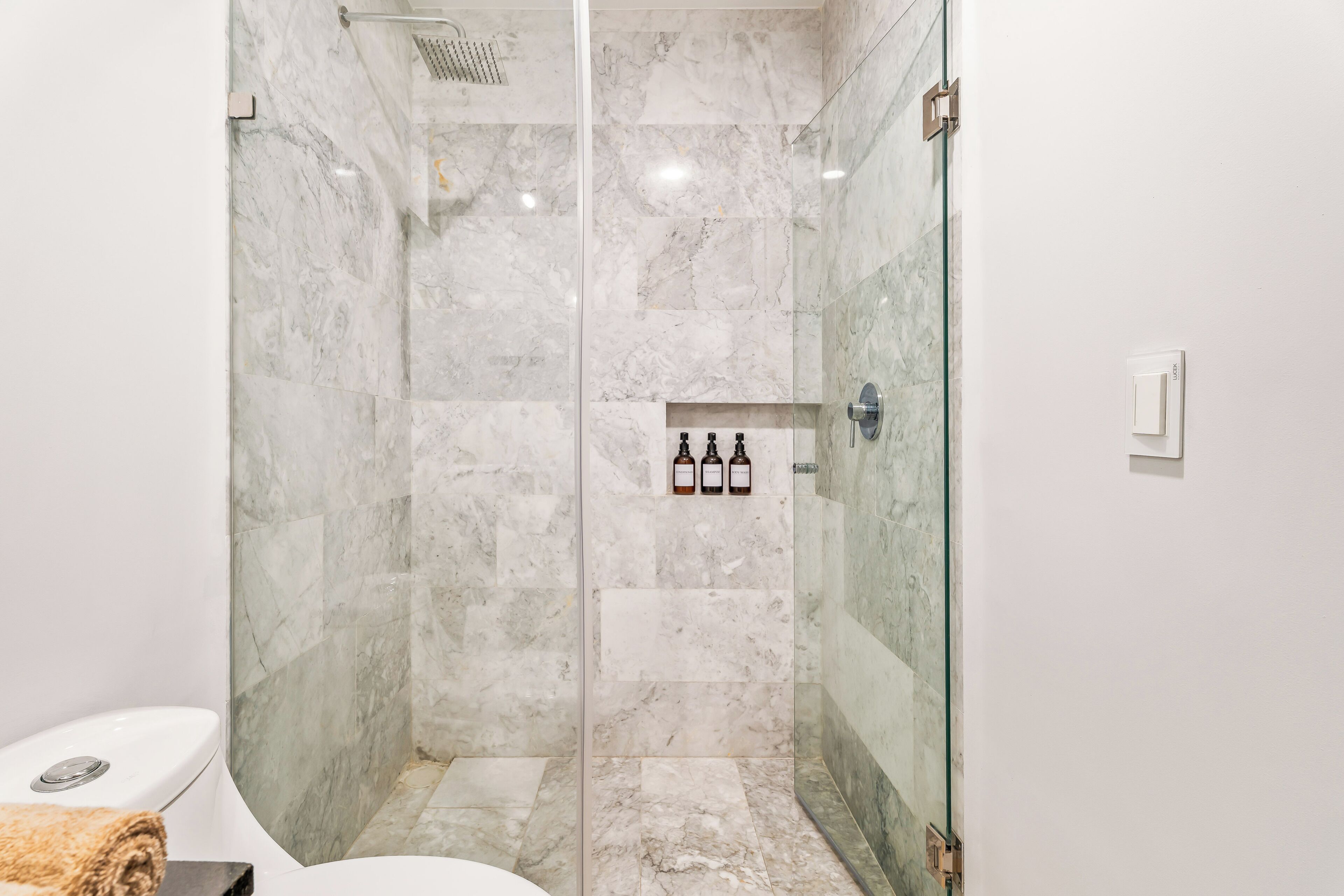 A modern bathroom with a glass-enclosed shower, marble tiles, and a toilet.