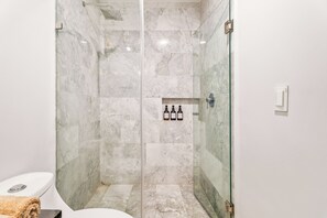 Une salle de bain moderne avec une douche à parois de verre, des carreaux de marbre et des toilettes.