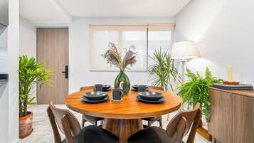 A dining area with a round wooden table, black chairs, a vase with dried plants, and a cabinet with a lamp.