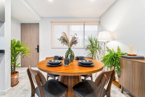 Un coin repas avec une table ronde en bois, des chaises noires, un vase contenant des plantes séchées et un meuble avec une lampe.
