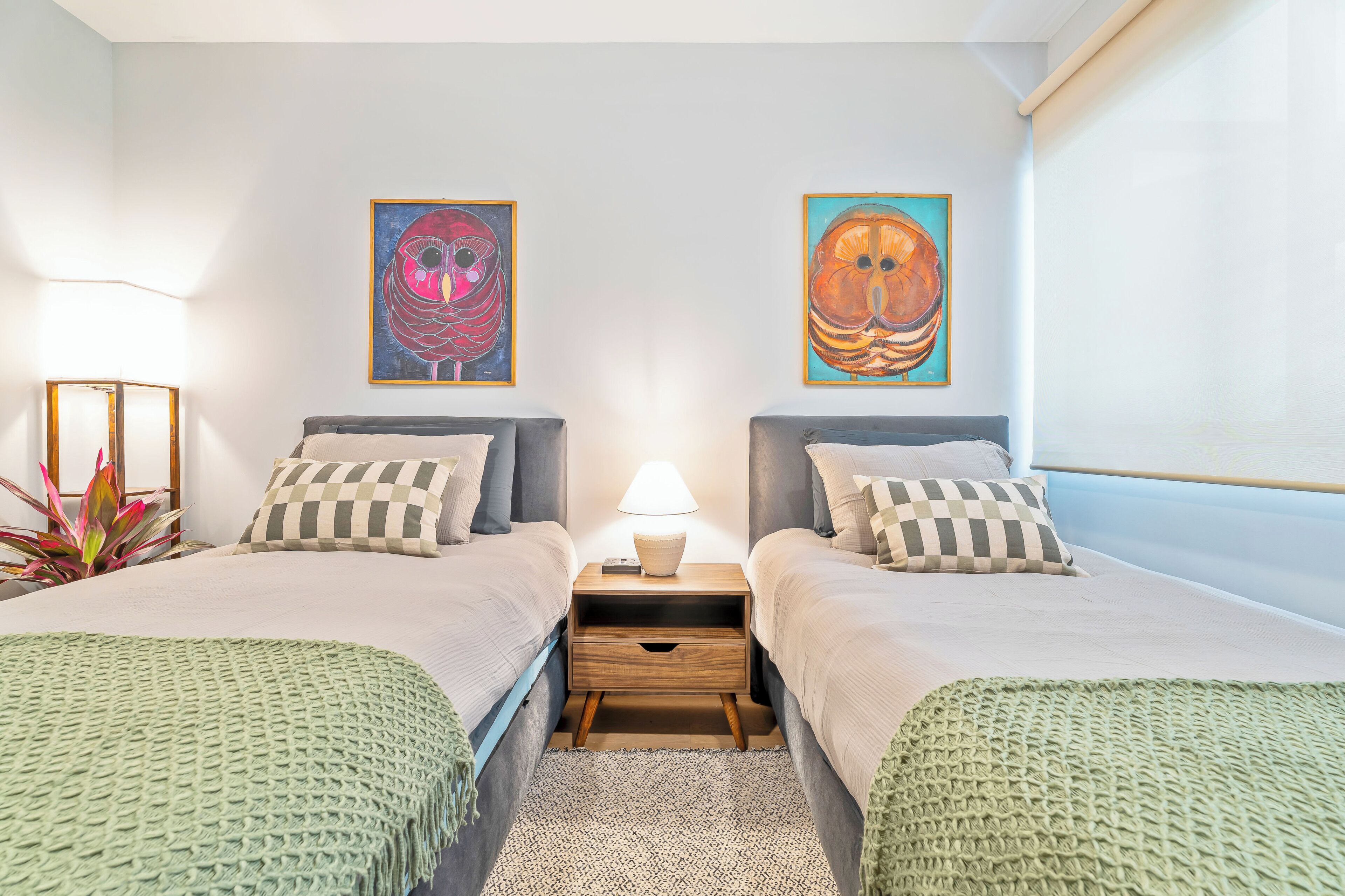 A double room with two beds, a nightstand with a lamp, and two wall-mounted paintings.