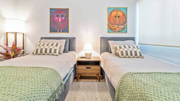 A double room with two beds, a nightstand with a lamp, and two wall-mounted paintings.