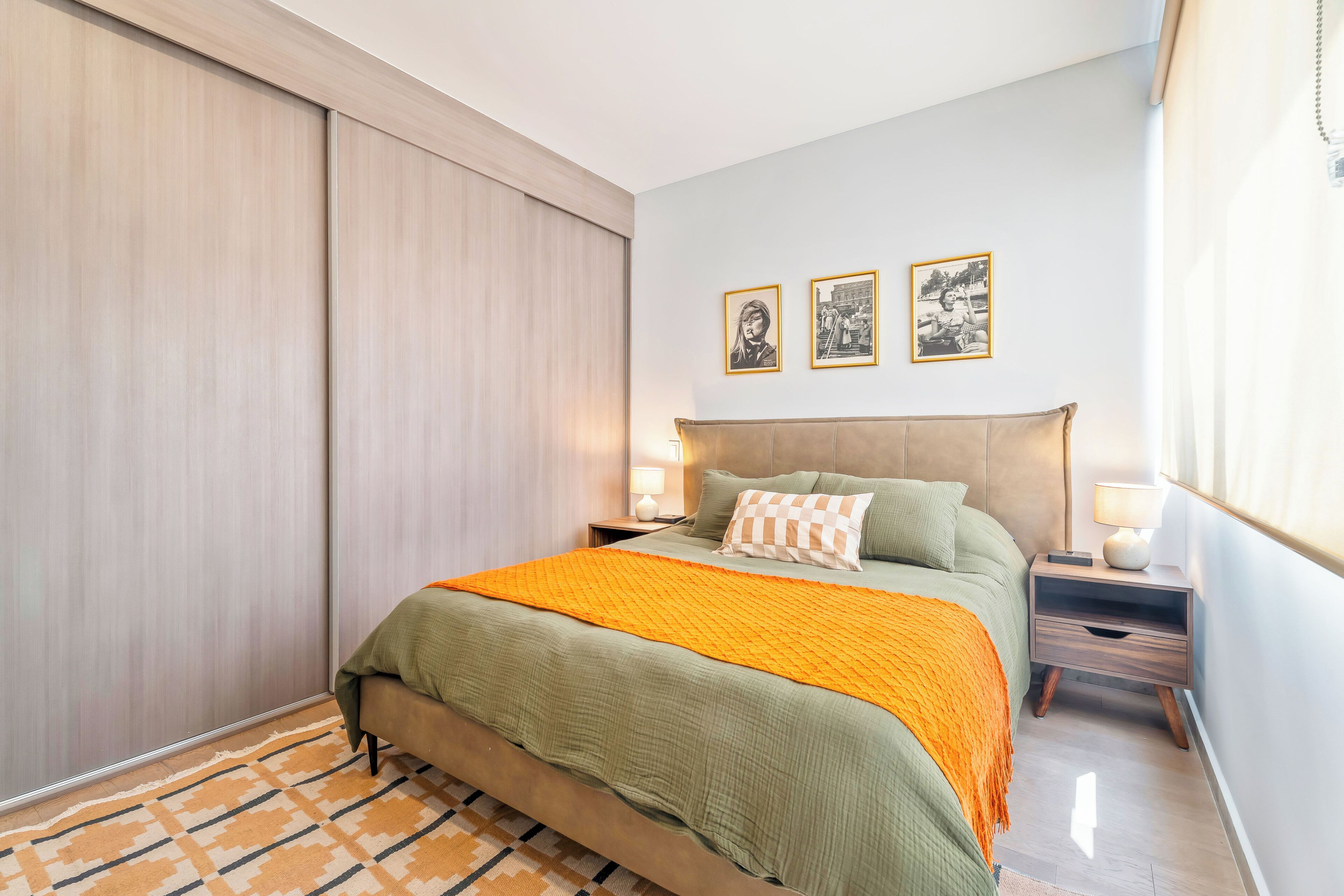 A bedroom with a bed, nightstands, a window, and a wall with framed pictures.