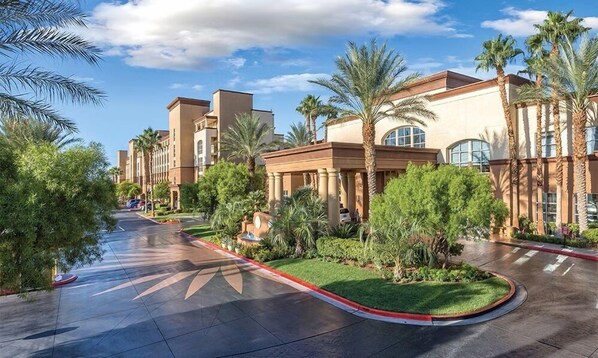 A hotel with a curved driveway, palm trees, and a clear sky.