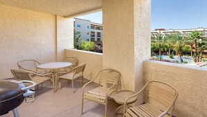 Un balcón con una parrilla, sillas y vistas a una piscina y edificios.