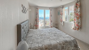 Une chambre à coucher avec un lit, une lampe, une fenêtre avec des rideaux et une vue sur l’extérieur.