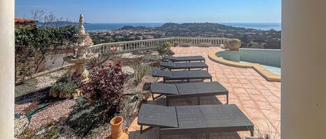 A terrace with outdoor seating, a decorative fountain, and a view of the coastline.