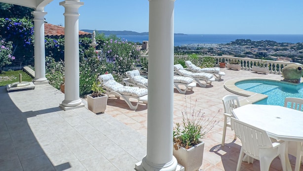Un espace aménagé au bord de la piscine, avec des chaises longues, une table et une vue sur la mer et le paysage urbain.