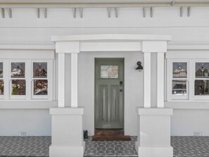 A white building with a green door, white columns, and patterned windows.