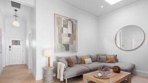 Een woonkamer met een bank, een salontafel, een lamp, een schilderij en een ronde spiegel aan de muur.