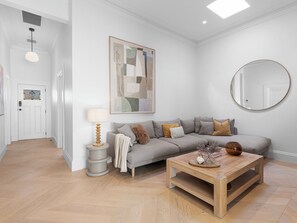A living room with a sofa, a coffee table, a lamp, a painting, and a round mirror on the wall.